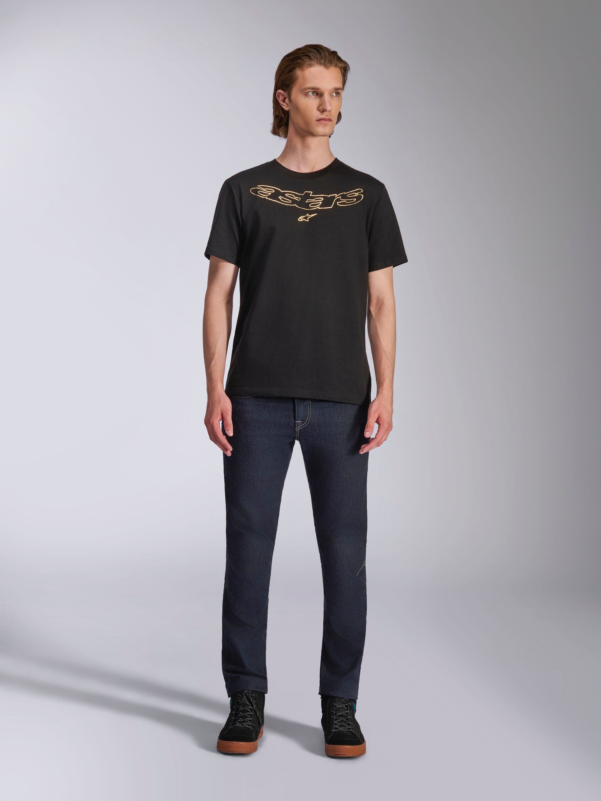 Alpinestars Luxo CSF Tee, t-shirt a maniche corte, nero, logo Astars sul petto profilato in tan, indossata da un modello con jeans in denim scuro e scarpe alte nere, abbigliamento casual motorsport streetwear