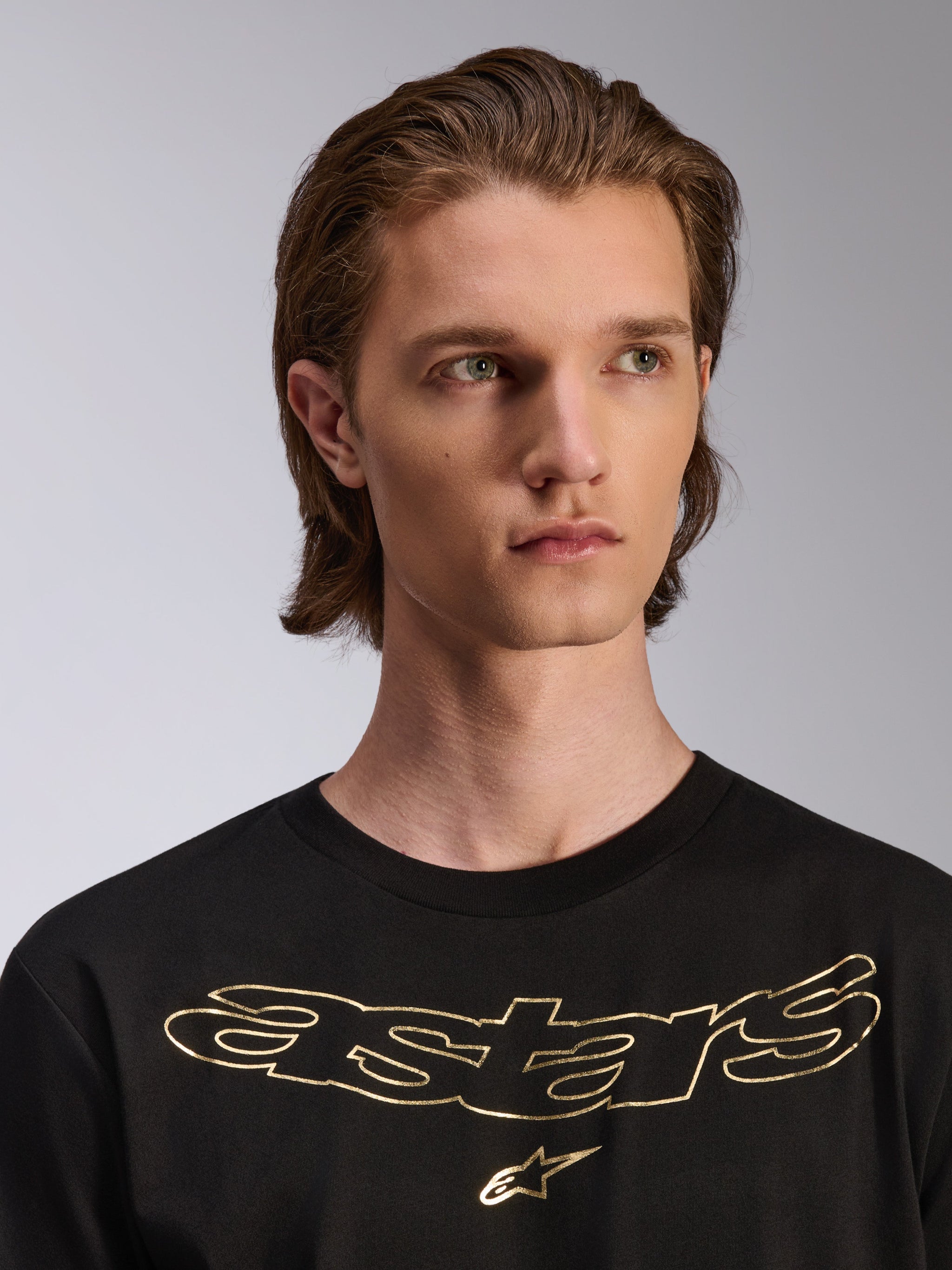 Alpinestars Luxo CSF Tee, maglietta a maniche corte, nero, logo Astars metallizzato oro sul petto, indossata da un modello, design casual ispirato al motorsport