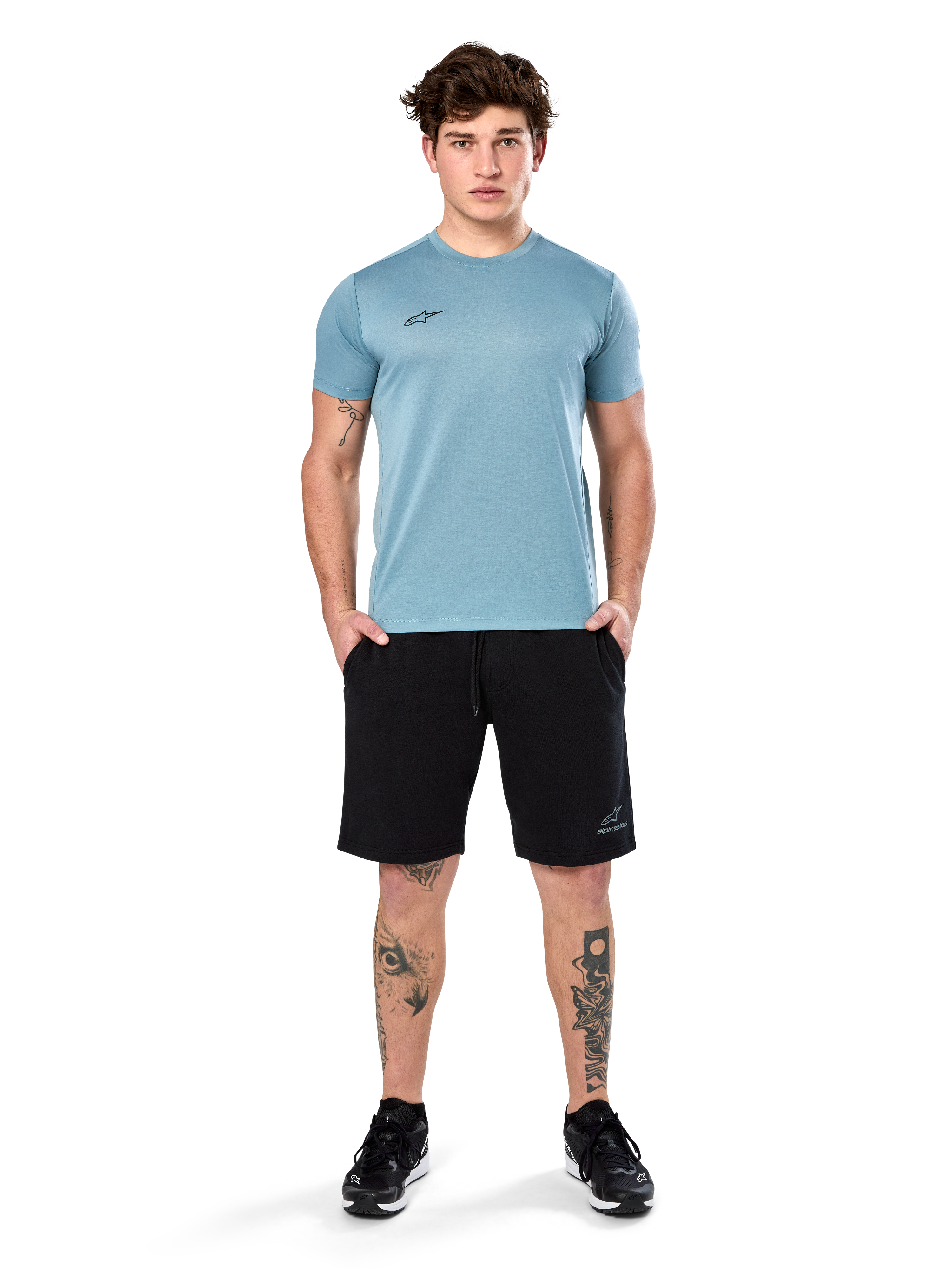 Alpinestars Point Performance Tee, t-shirt a maniche corte, blu ghiaccio, con un piccolo logo nero sul davanti, girocollo, indossata da un modello con pantaloncini neri e sneakers nere, abbigliamento sportivo casual traspirante
