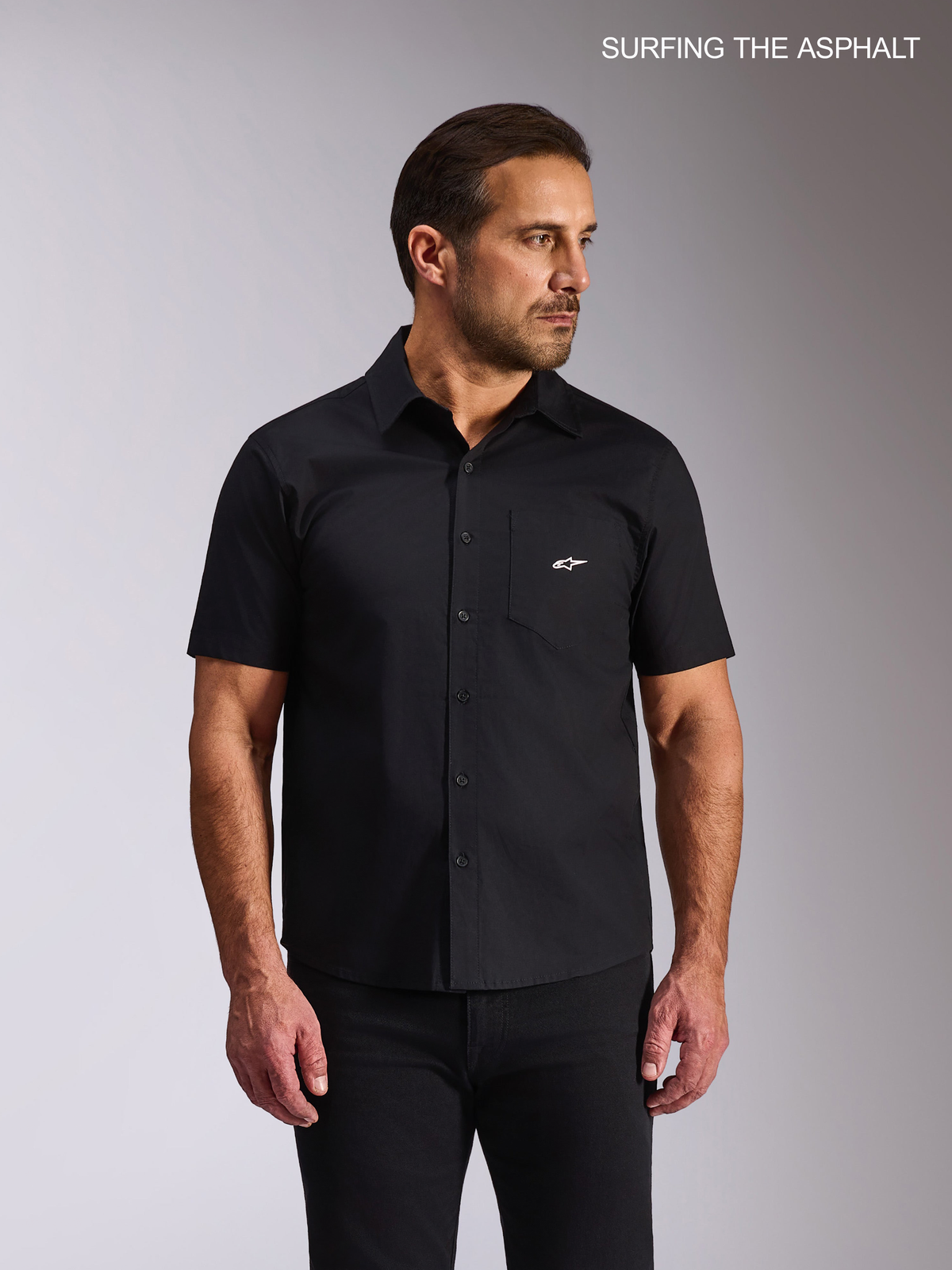 Alpinestars Camicia Strive Woven, camicia casual a maniche corte da uomo, nero, in popeline elasticizzato, con taschino e logo bianco sul petto, indossata da un modello