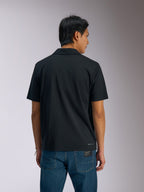 Alpinestars Impetus Sport Polo, polo a maniche corte nera, vista posteriore di un uomo che indossa la polo con jeans in denim blu, con piccola scritta Alpinestars sulla parte inferiore della schiena, abbigliamento sportivo casual ispirato al motorsport