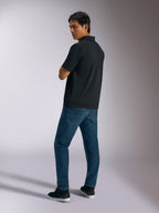 Alpinestars Impetus Sport Polo, polo a maniche corte nera in tessuto finta rete con chiusura a tre bottoni, indossata da un modello con jeans blu e sneakers nere, streetwear casual ispirato al motorsport