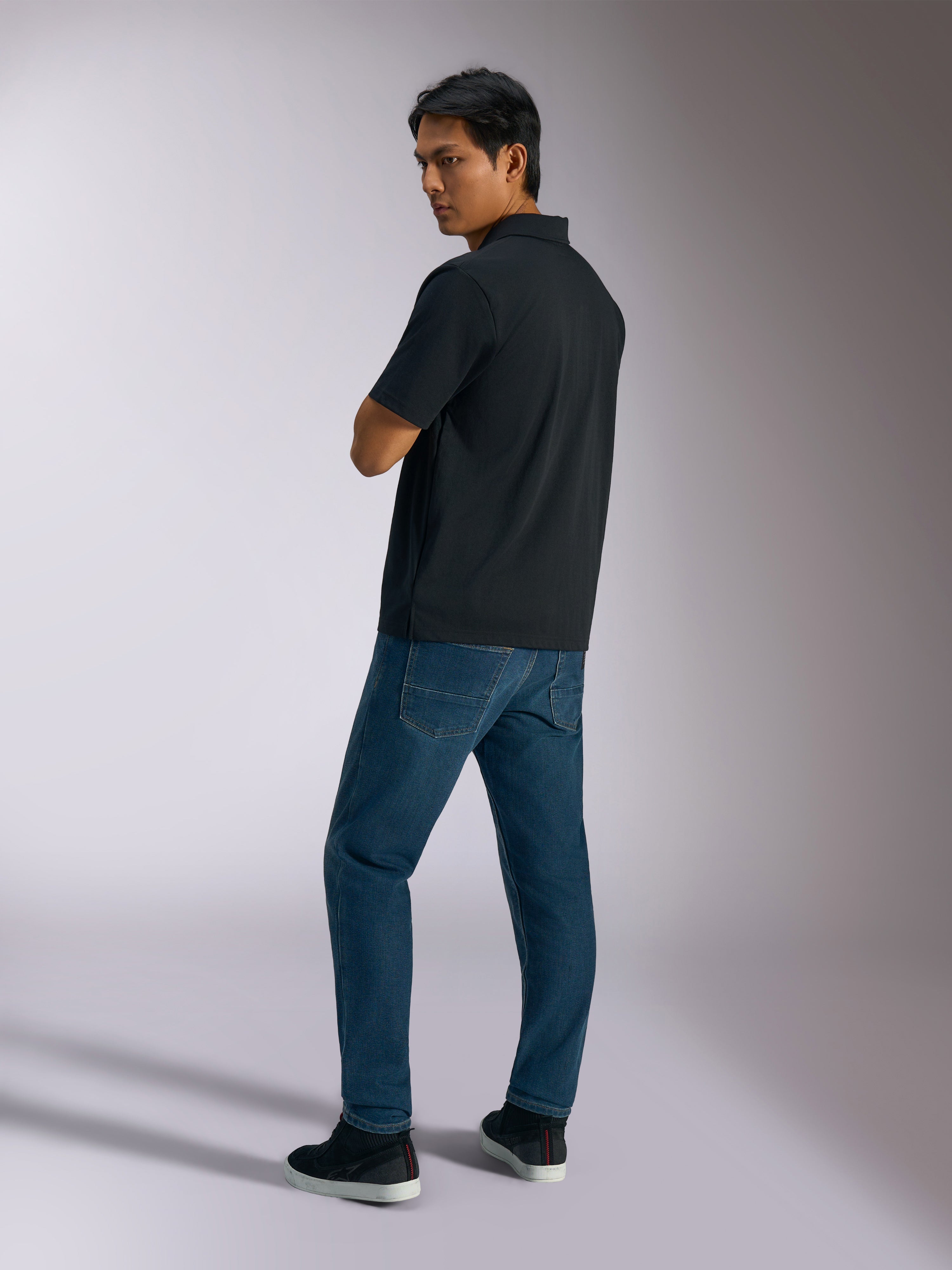 Alpinestars Impetus Sport Polo, polo a maniche corte nera in tessuto finta rete con chiusura a tre bottoni, indossata da un modello con jeans blu e sneakers nere, streetwear casual ispirato al motorsport