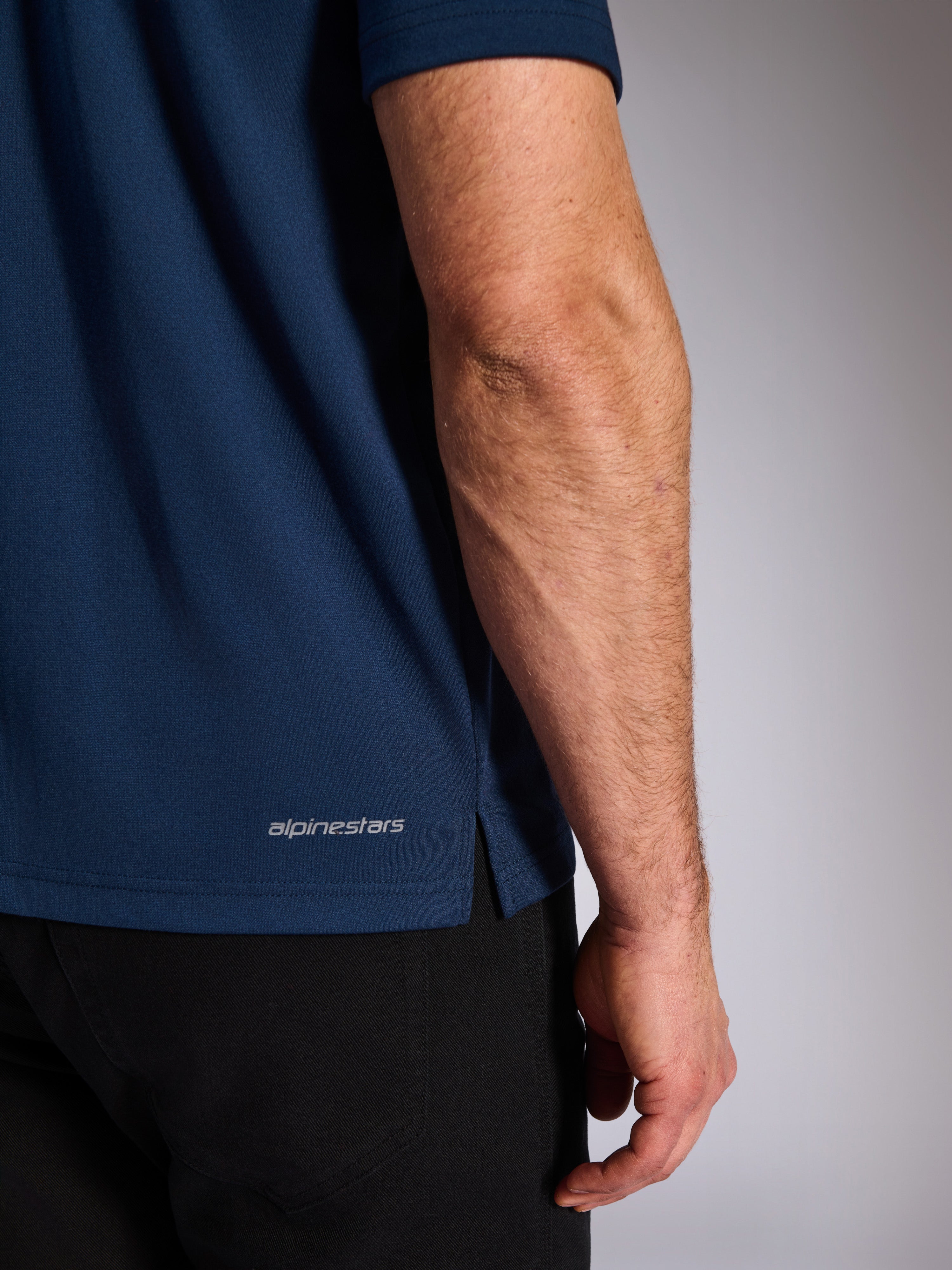 Alpinestars Impetus Sport Polo, Navy, primo piano dell'orlo inferiore con scritta Alpinestars e spacco laterale, trama in maglia a rete finta, abbigliamento sportivo casual da motorsport