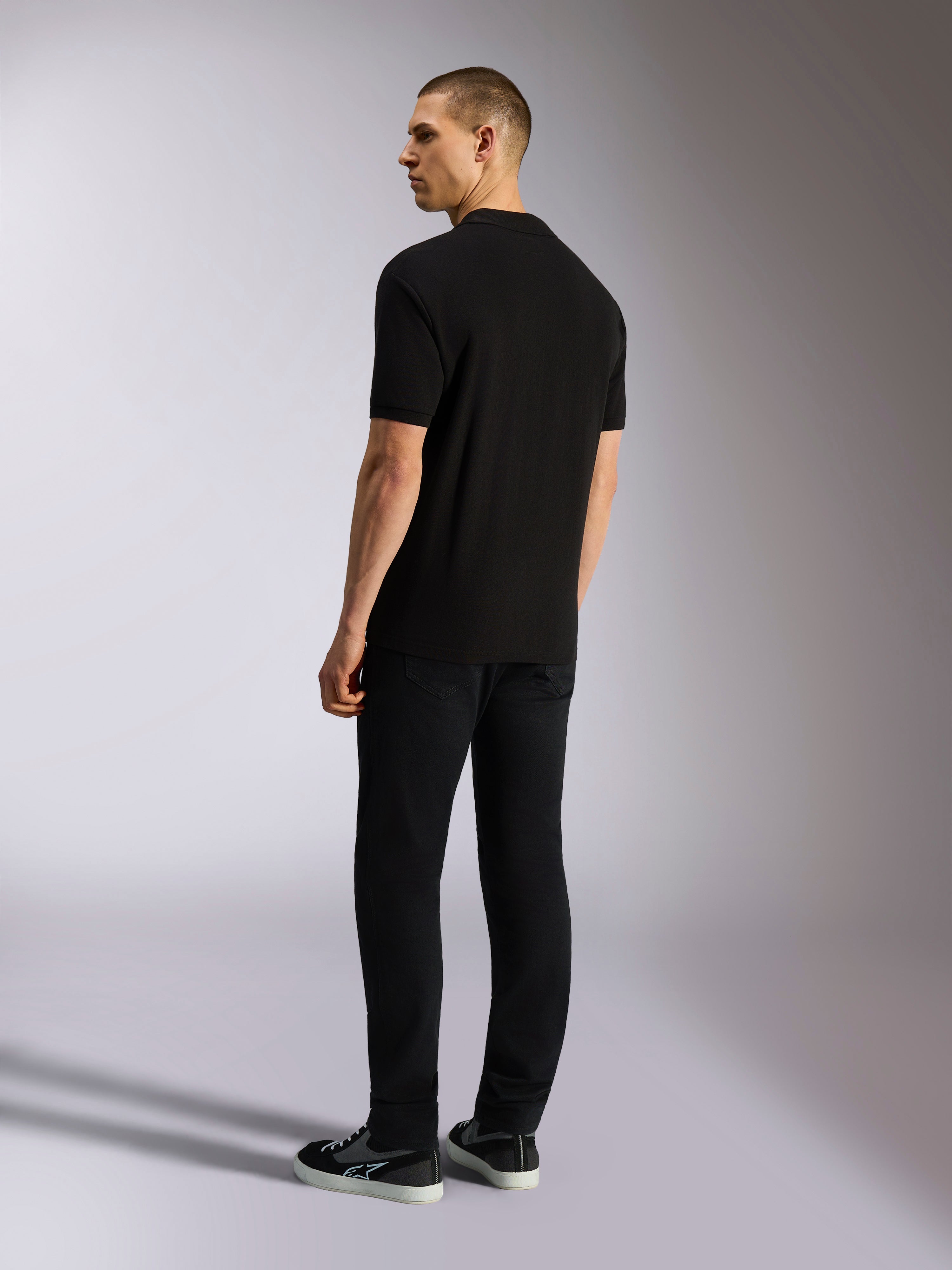Polo Alpinestars Endeavor Classic, polo in piqué a maniche corte, nero, vista posteriore di un modello maschile con pantaloni neri e sneakers, streetwear casual ispirato al motorsport