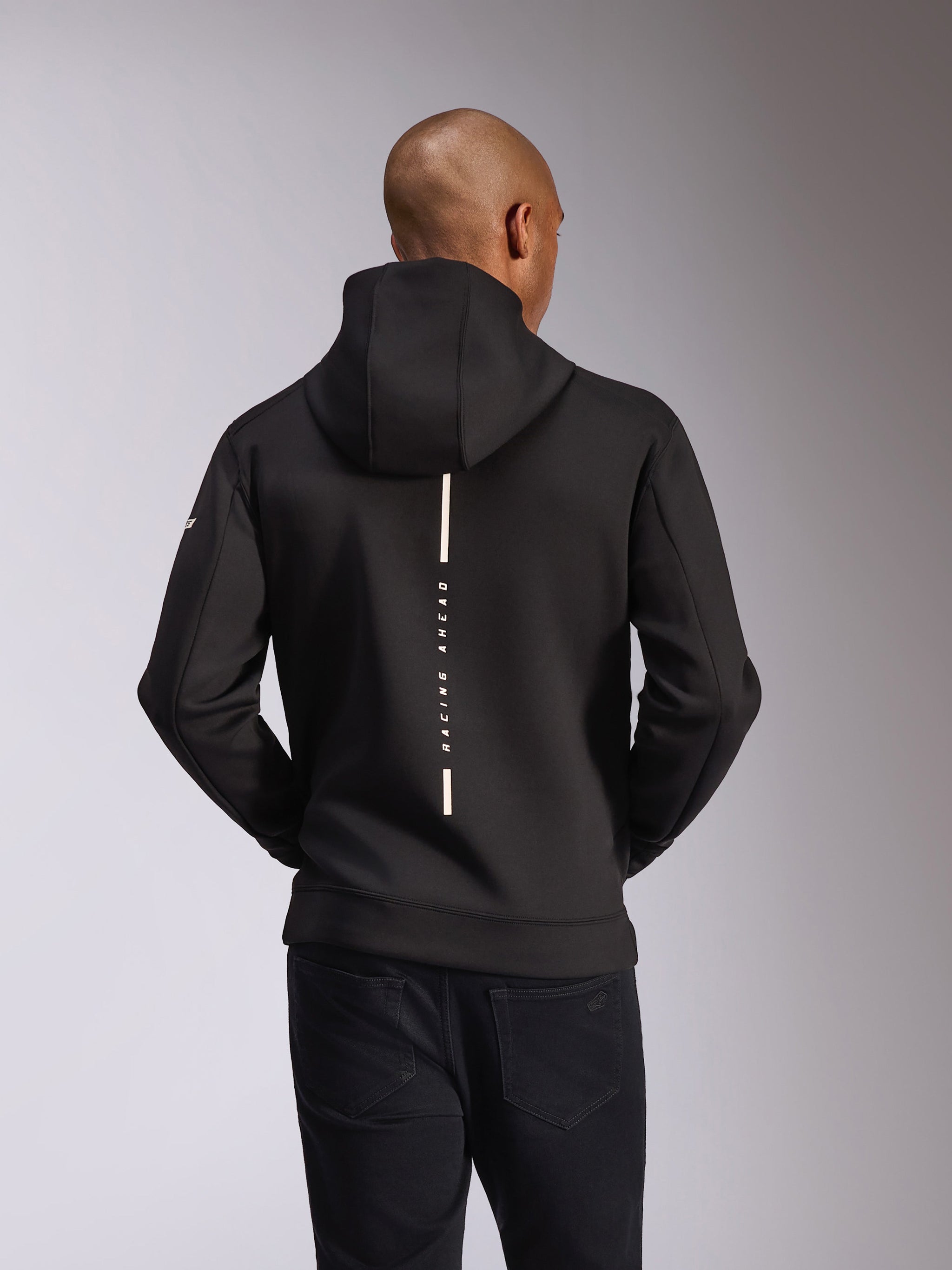Felpa con cappuccio Alpinestars Insight, vista posteriore, nera, striscia bianca verticale con scritta 'RACING AHEAD', logo testuale sulla manica, streetwear casual ispirato al motorsport