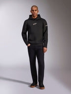 Alpinestars Insight Hoodie, felpa nera con cappuccio e logo Astars bianco sul petto e sulla manica, indossata da un modello con pantaloni neri e sneakers nere, streetwear casual ispirato al motorsport