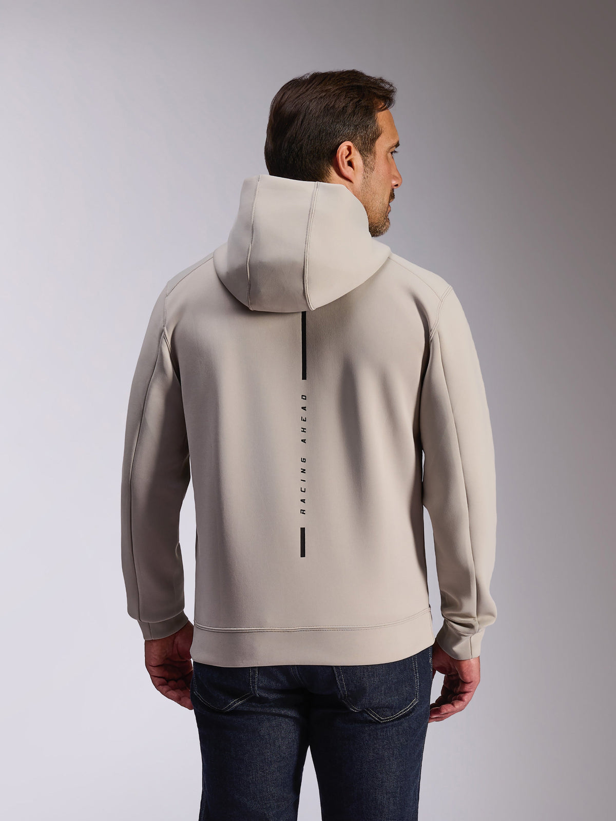 Alpinestars Felpa Insight Hoodie in Cement, vista posteriore di un modello che indossa una felpa pullover grigio chiaro, con logo a striscia verticale nera e scritta 'RACING AHEAD', felpa casual in pile double face ispirata al motorsport