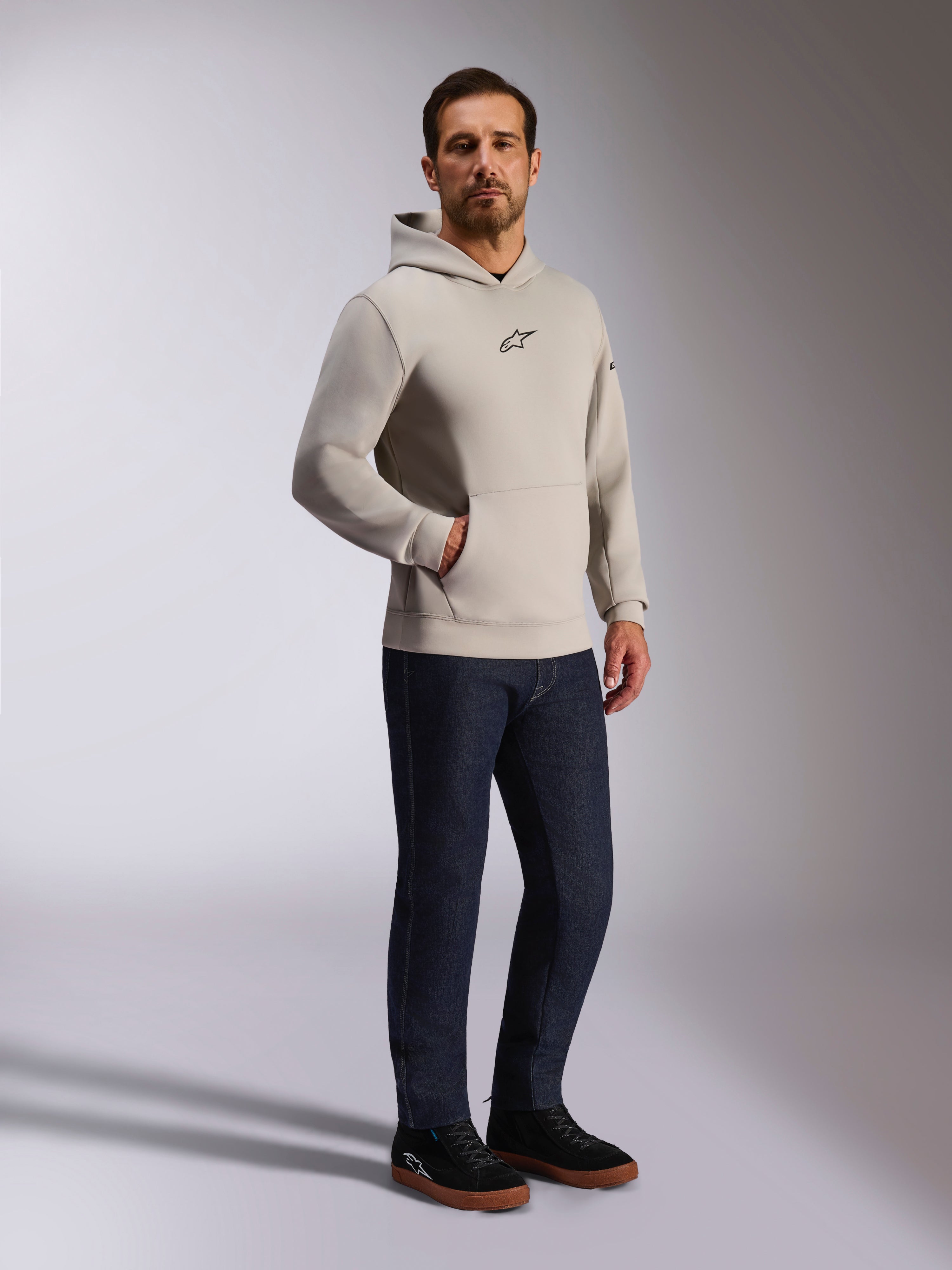 Felpa con cappuccio Alpinestars Insight, streetwear casual, grigio cemento con logo Astars nero sul petto, modello pullover con tasca a marsupio, indossata con jeans blu scuro e sneakers nere, stile moderno ispirato al motorsport