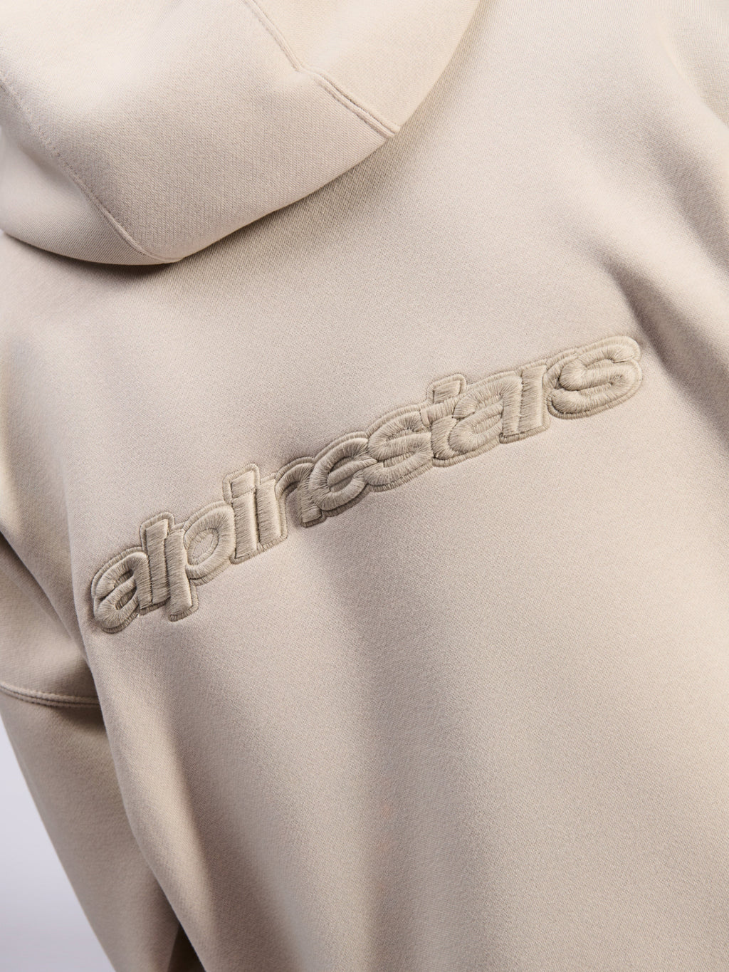 Felpa con cappuccio Alpinestars Emergent Oversized, streetwear casual, colore sabbia, vista dettagliata del logo Alpinestars con ricamo 3D tono su tono sul retro, texture in pile premium