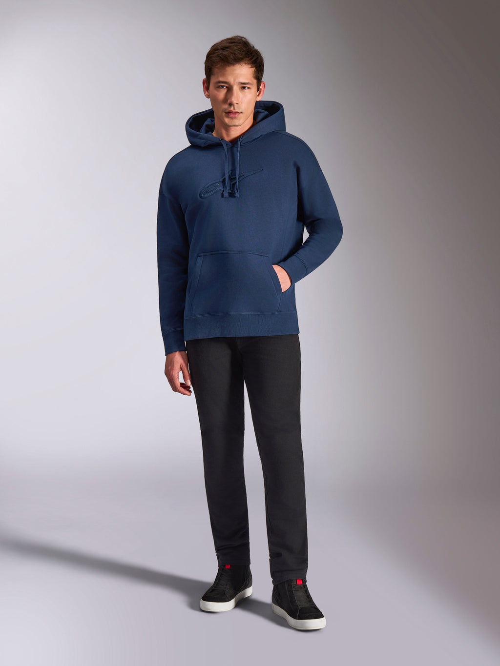 Felpa con cappuccio Alpinestars Emergent Oversized, felpa pullover blu navy, logo ricamato 3D tono su tono sul petto, indossata da un modello con pantaloni neri e sneakers, stile streetwear casual