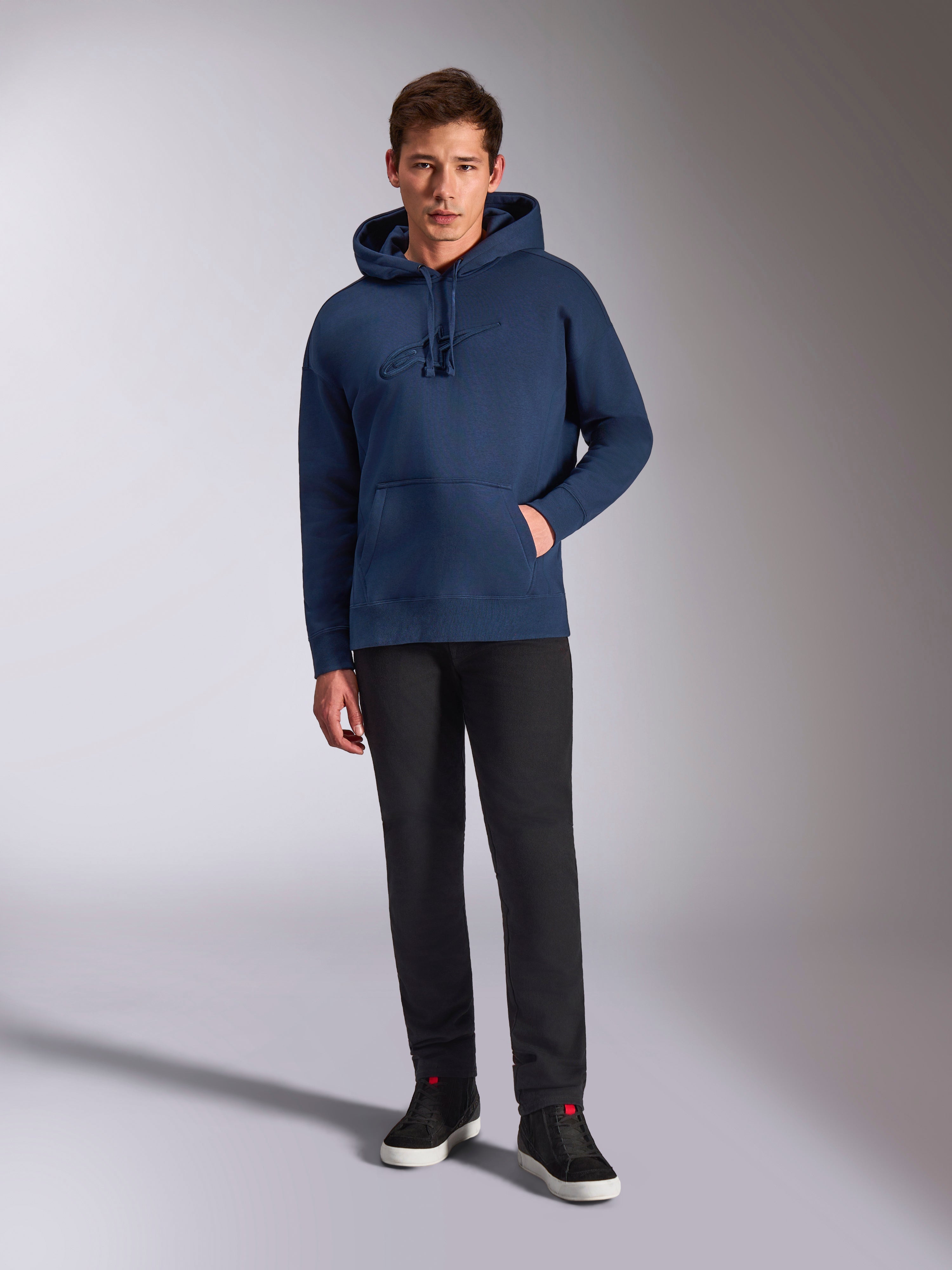 Felpa con cappuccio Alpinestars Emergent Oversized, felpa pullover blu navy, logo ricamato 3D tono su tono sul petto, indossata da un modello con pantaloni neri e sneakers, stile streetwear casual