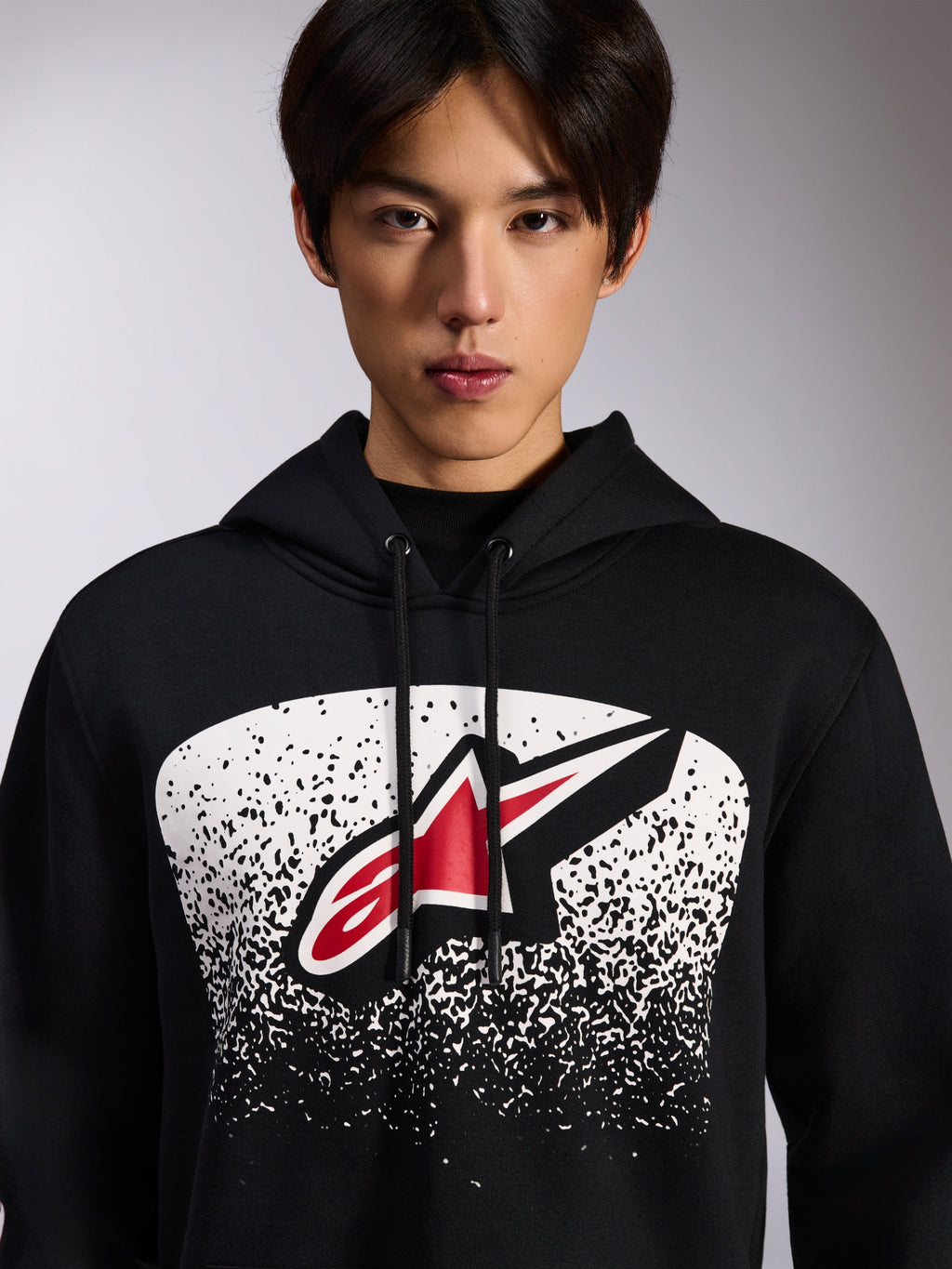 Alpinestars Obsessed Hoodie, felpa nera con cappuccio, con logo Astars rosso e bianco all'interno di una grafica bianca a gradazione puntinata MX sul petto, indossata da un modello, abbigliamento streetwear casual da motorsport con cappuccio regolabile con cordino