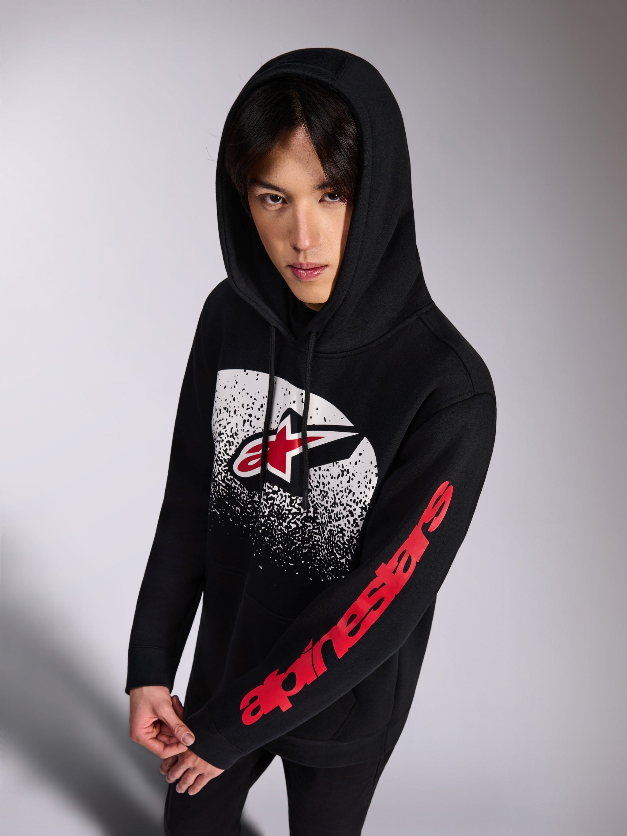 Alpinestars Obsessed Hoodie, felpa pullover nera, logo Astars frontale rosso e bianco con gradazione MX bianca effetto consumato, scritta Alpinestars rossa sulla manica, cappuccio con cordino, streetwear casual ispirato al motorsport