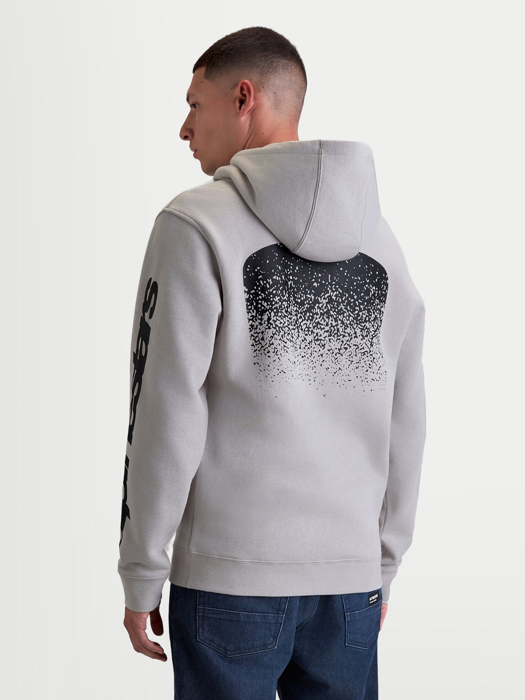 Alpinestars Felpa con cappuccio Obsessed, felpa in pile sportswear da uomo, grigio cemento, con grande grafica posteriore sfumata nera ispirata all'MX e logo sulla manica, vista posteriore su modello, abbigliamento casual motorsport.