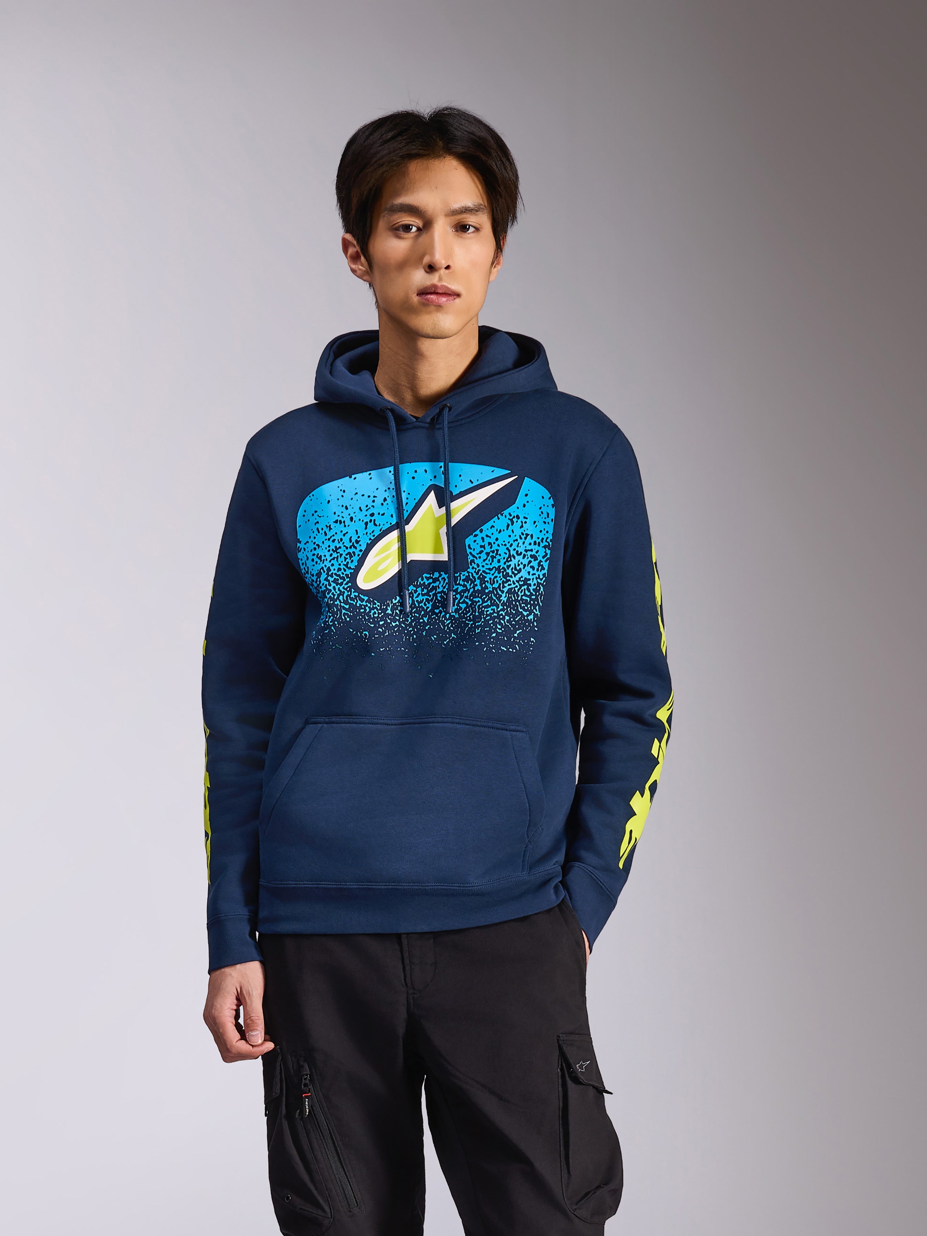 Felpa con cappuccio Alpinestars Obsessed in blu navy, indossata da un modello uomo, con logo Astars verde lime e gradazione MX blu acceso sul petto e loghi gialli sulle maniche, streetwear casual ispirato al motorsport