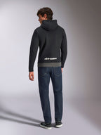 Felpa con cappuccio Alpinestars Parallel, vista posteriore di un uomo che indossa un pullover in pile a blocchi di colore nero e gunmetal, logo Alpinestars bianco sulla parte inferiore della schiena, abbinata a jeans blu scuro, streetwear casual ispirato al motorsport