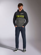 Alpinestars Parallel Hoodie, felpa con cappuccio a blocchi di colore, nero e grigio gunmetal, logo Alpinestars giallo acceso e logo a stella bianco sul petto, indossata da un modello con jeans blu scuro e sneakers nere, streetwear casual motorsport