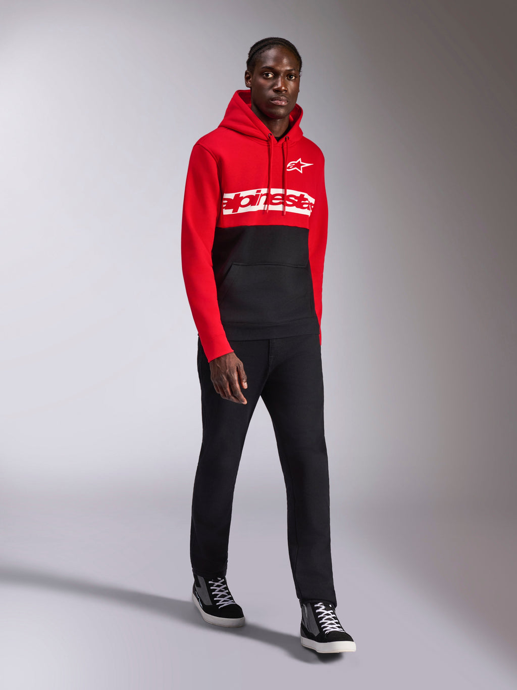 Alpinestars Parallel Hoodie, sportswear casual, design a blocchi di colore rosso e nero, con marchio Alpinestars bianco e logo a stella sul petto, indossata con pantaloni neri e sneakers, look moderno ispirato al motorsport