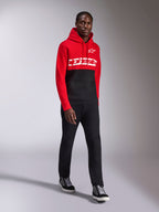 Alpinestars Parallel Hoodie, sportswear casual, design a blocchi di colore rosso e nero, con marchio Alpinestars bianco e logo a stella sul petto, indossata con pantaloni neri e sneakers, look moderno ispirato al motorsport
