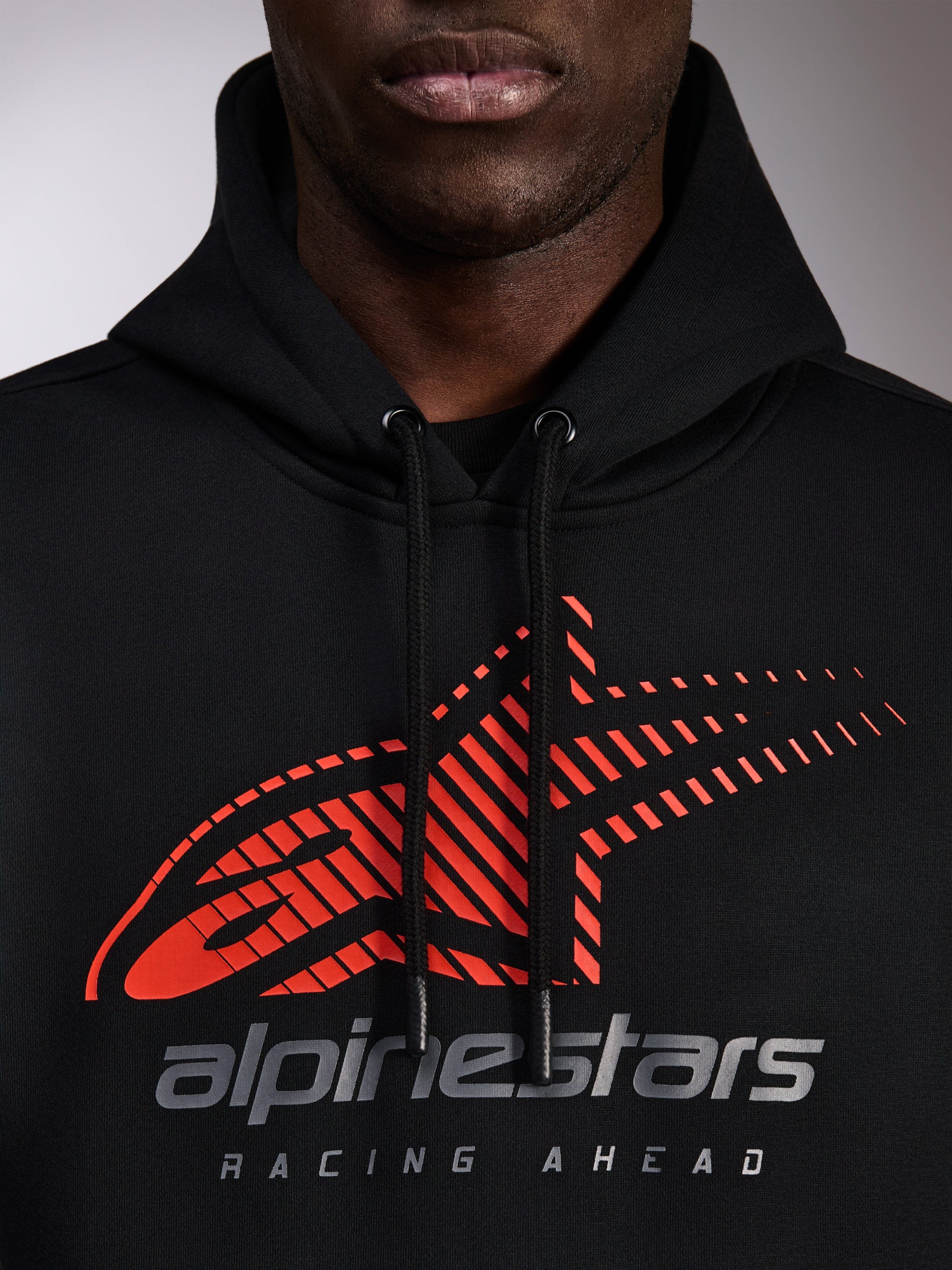 Alpinestars Pulse Hoodie, felpa nera con cappuccio, primo piano del petto con logo Astars rosso con linee di velocità sfumate e marchio argento, cordini neri con estremità immerse, streetwear casual motorsport