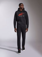 Alpinestars Pulse Hoodie, felpa con cappuccio casual streetwear nera, logo Astars combo rosso e grigio con linea di velocità sfumata sul petto, cappuccio con cordino, tasca a marsupio anteriore, maniche lunghe, abbinata a pantaloni neri e sneakers, design ispirato al motorsport