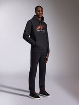 Alpinestars Pulse Hoodie, felpa nera con cappuccio, con logo Astars rosso e bianco, linea di velocità sfumata e scritta Racing Ahead, indossata con pantaloni e sneaker neri coordinati, streetwear casual ispirato al motorsport.