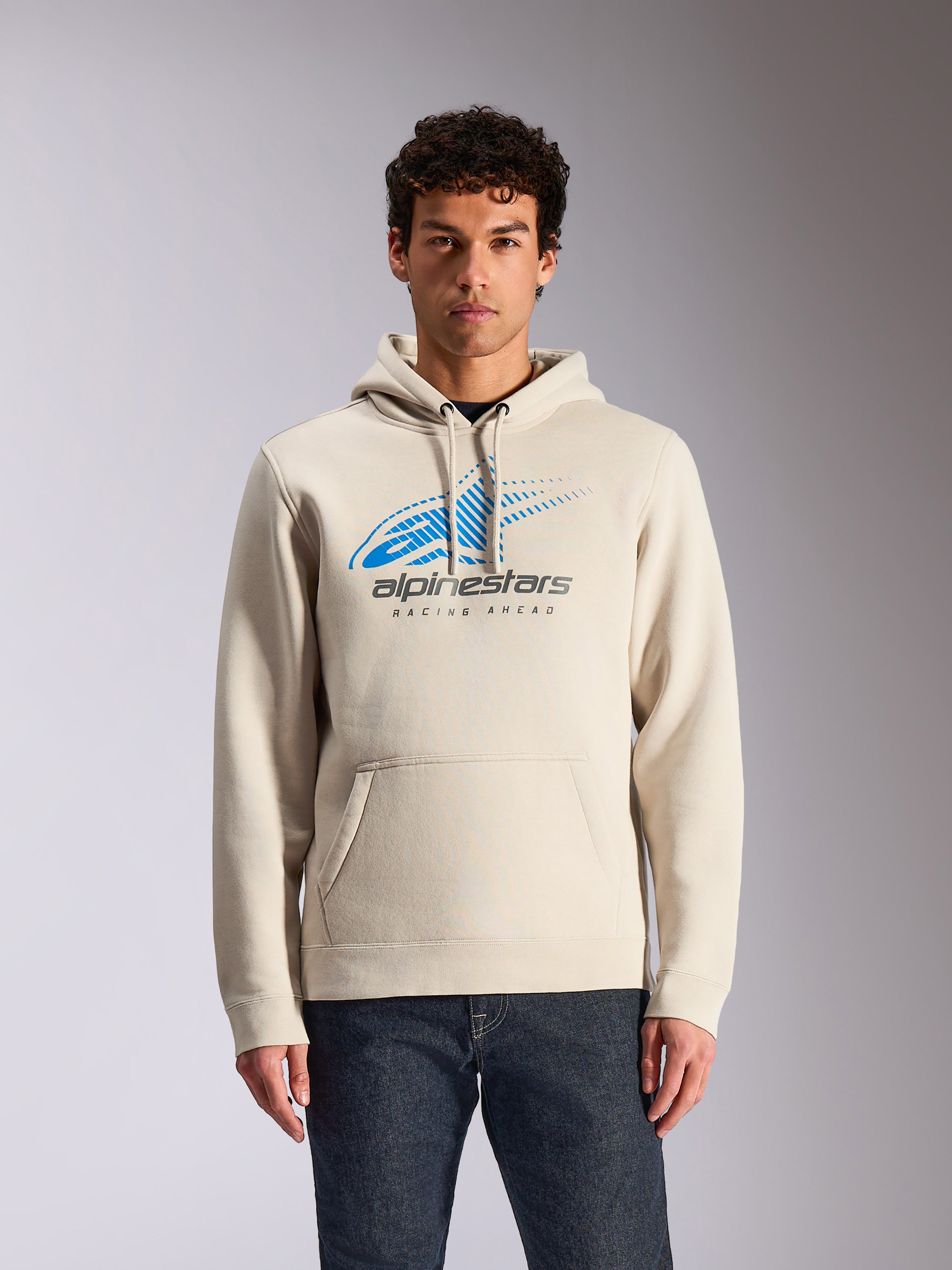 Alpinestars Pulse Hoodie, felpa casual con cappuccio bianco sporco, logo Astars Combo frontale blu e grigio con grafica sfumata a linee di velocità, tasca a marsupio frontale, indossata da un modello con jeans scuri, streetwear ispirato al motorsport