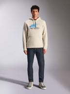 Felpa con cappuccio Alpinestars Pulse, bianco sporco, pullover a maniche lunghe con cappuccio e cordino, logo Astars Combo blu e nero con linea di velocità sfumata, abbinata a jeans scuri e sneakers, streetwear casual motorsport