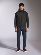 Modello con felpa Alpinestars Cypher Hoodie, felpa in pile nera con zip frontale, cappuccio a collo alto e piccolo logo Astars bianco sul petto, abbinata a jeans scuri e sneakers nere, stile streetwear casual ispirato al motorsport