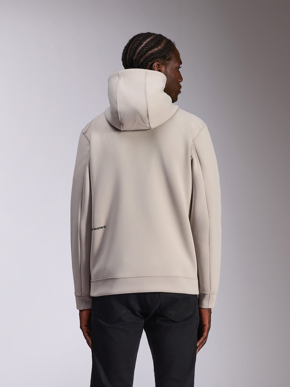 Felpa con cappuccio Alpinestars Cypher, abbigliamento sportivo casual, grigio Cement, vista posteriore su modello, cappuccio a collo alto, materiale in pile double-face, logo Alpinestars minimale sulla parte inferiore della schiena, abbinata a pantaloni neri