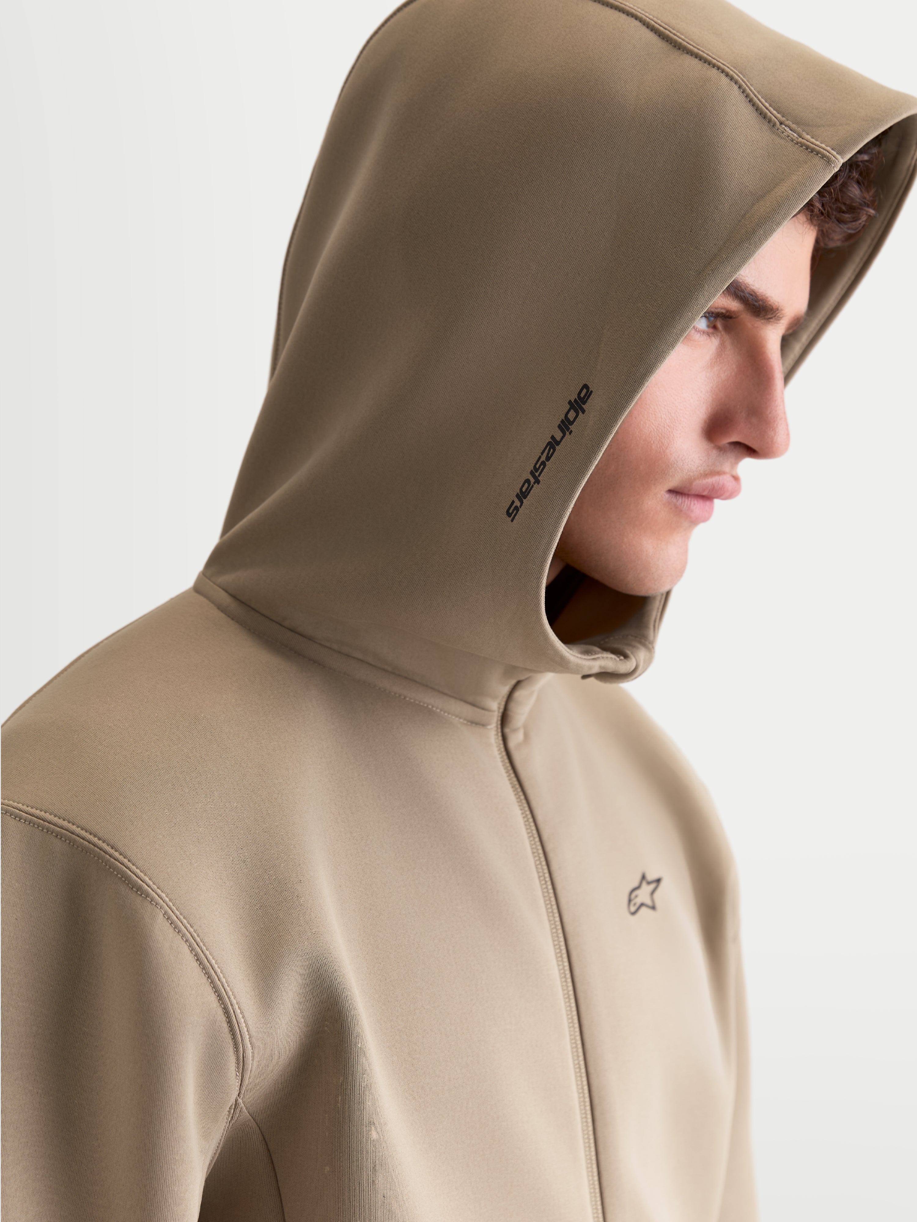 Alpinestars Felpa con cappuccio Cypher, felpa in pile sportswear con zip frontale da uomo, beige, con cappuccio a collo alto foderato in rete, marchio Alpinestars laterale e logo sul petto, vista di profilo su modello.