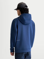 Alpinestars felpa con cappuccio Cypher, felpa sportiva in pile blu, vista posteriore su modello che mostra il cappuccio a collo alto foderato in rete e il discreto logo Alpinestars sulla parte inferiore della schiena, tessuto tri-blend di alta qualità per uno stile casual ispirato al motorsport