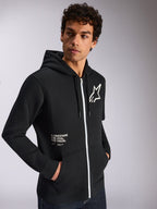 Alpinestars Felpa con cappuccio Transverse, abbigliamento sportivo casual, nero con dettaglio zip bianco, cappuccio con cordino, logo Alpinestars sul petto, grafica 'One Goal One Vision', indossata da un modello con capelli scuri e ricci