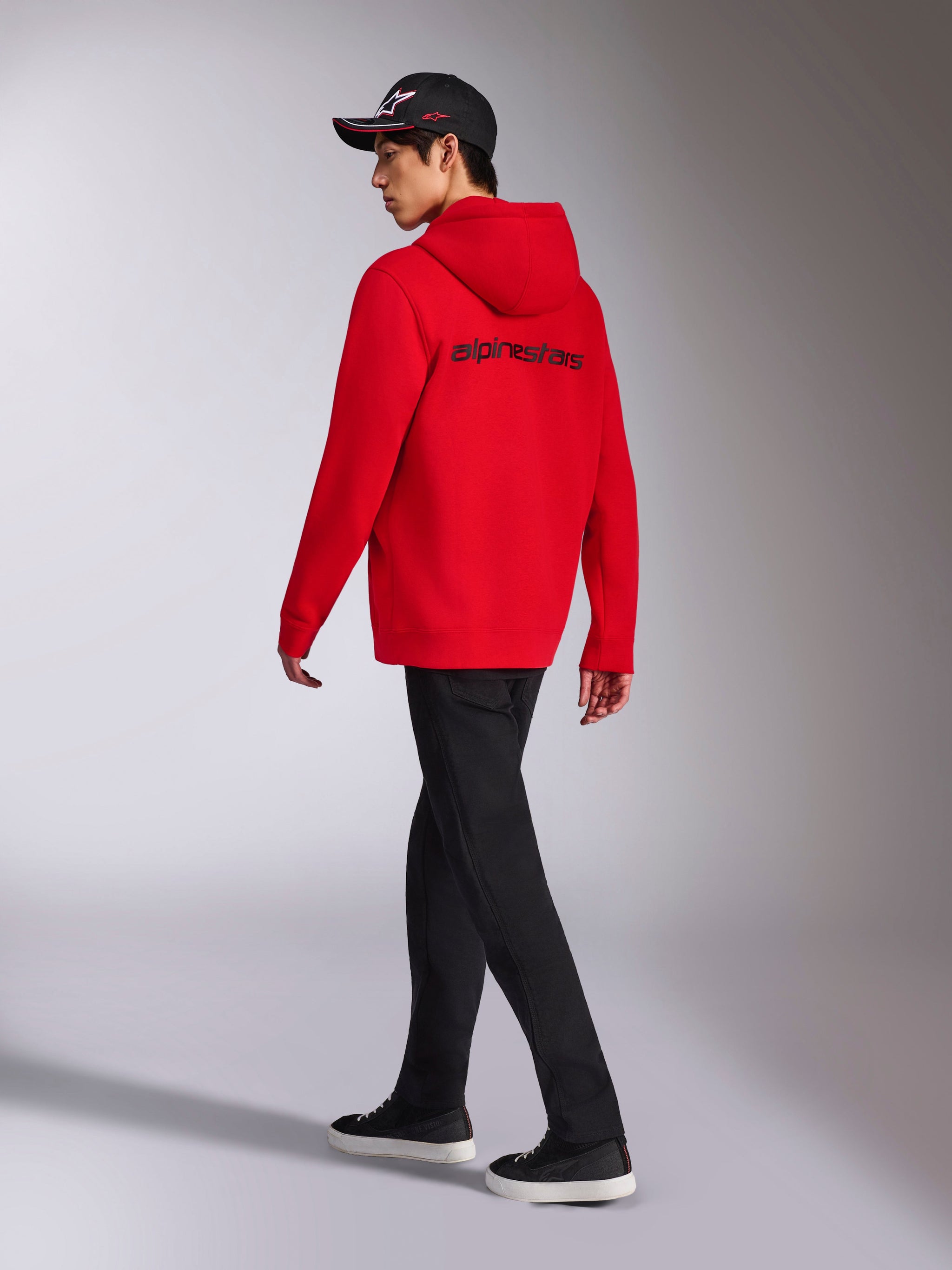 Felpa con cappuccio Alpinestars Transverse, felpa in pile rossa con zip, vista posteriore con logo Alpinestars nero, indossata da un modello con pantaloni neri e cappellino nero con logo, streetwear casual ispirato al motorsport
