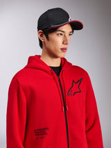 Alpinestars Transverse Hoodie, felpa rossa con zip frontale, logo Astars nero sul petto e testo 'One Goal. One Vision.' sulla parte inferiore frontale, streetwear casual motorsport, indossata da un modello con cappellino nero