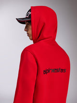 Felpa con cappuccio Alpinestars Transverse, felpa rossa, vista laterale-posteriore che mostra il logo Alpinestars nero sul retro, indossata con il cappuccio alzato e un cappellino nero, streetwear casual ispirato al motorsport