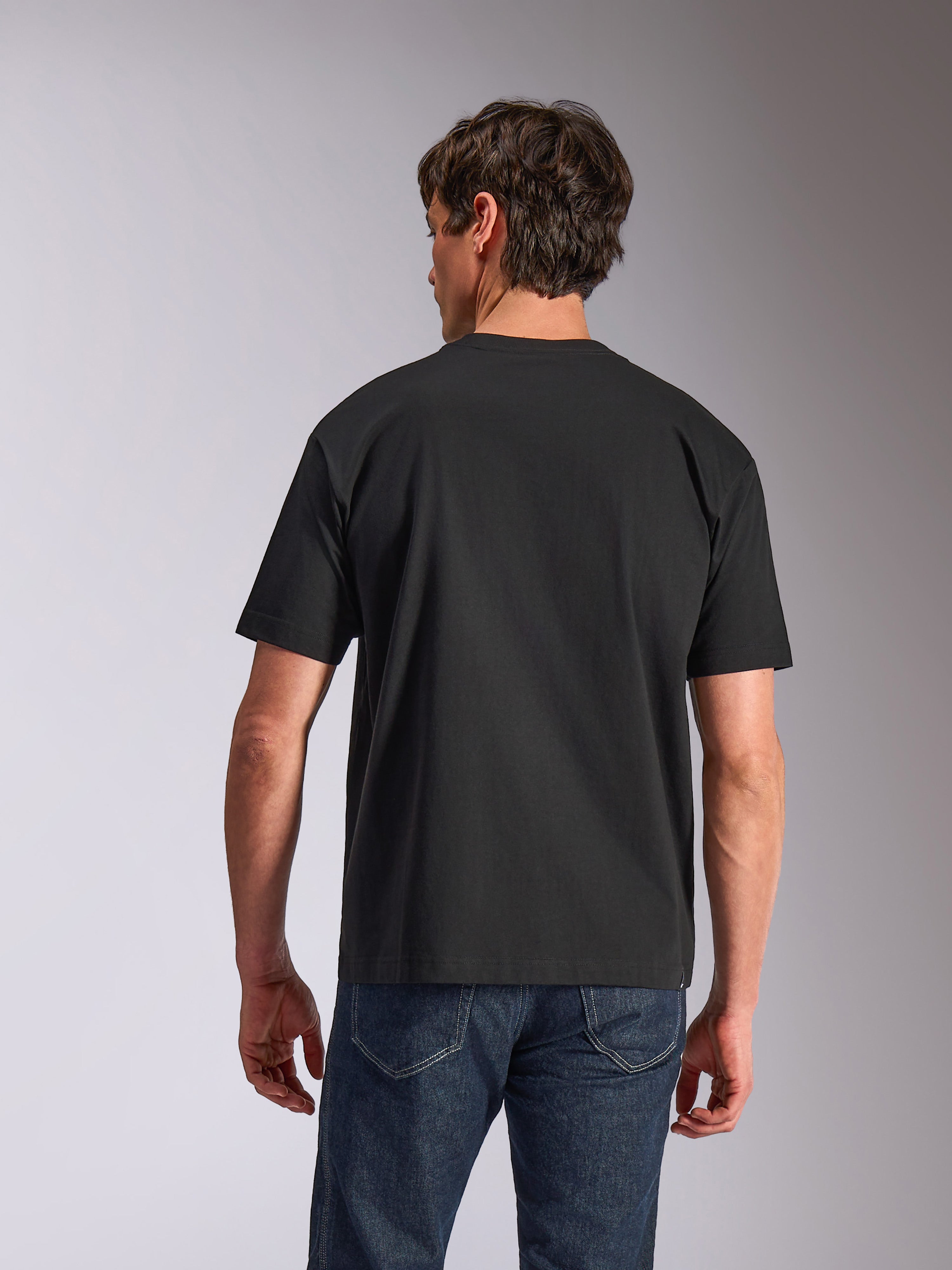 Alpinestars Aplomb Oversized CSF Tee, t-shirt a maniche corte, nero, vista posteriore, indossata da un modello con jeans blu, abbigliamento sportivo casual dalla vestibilità rilassata