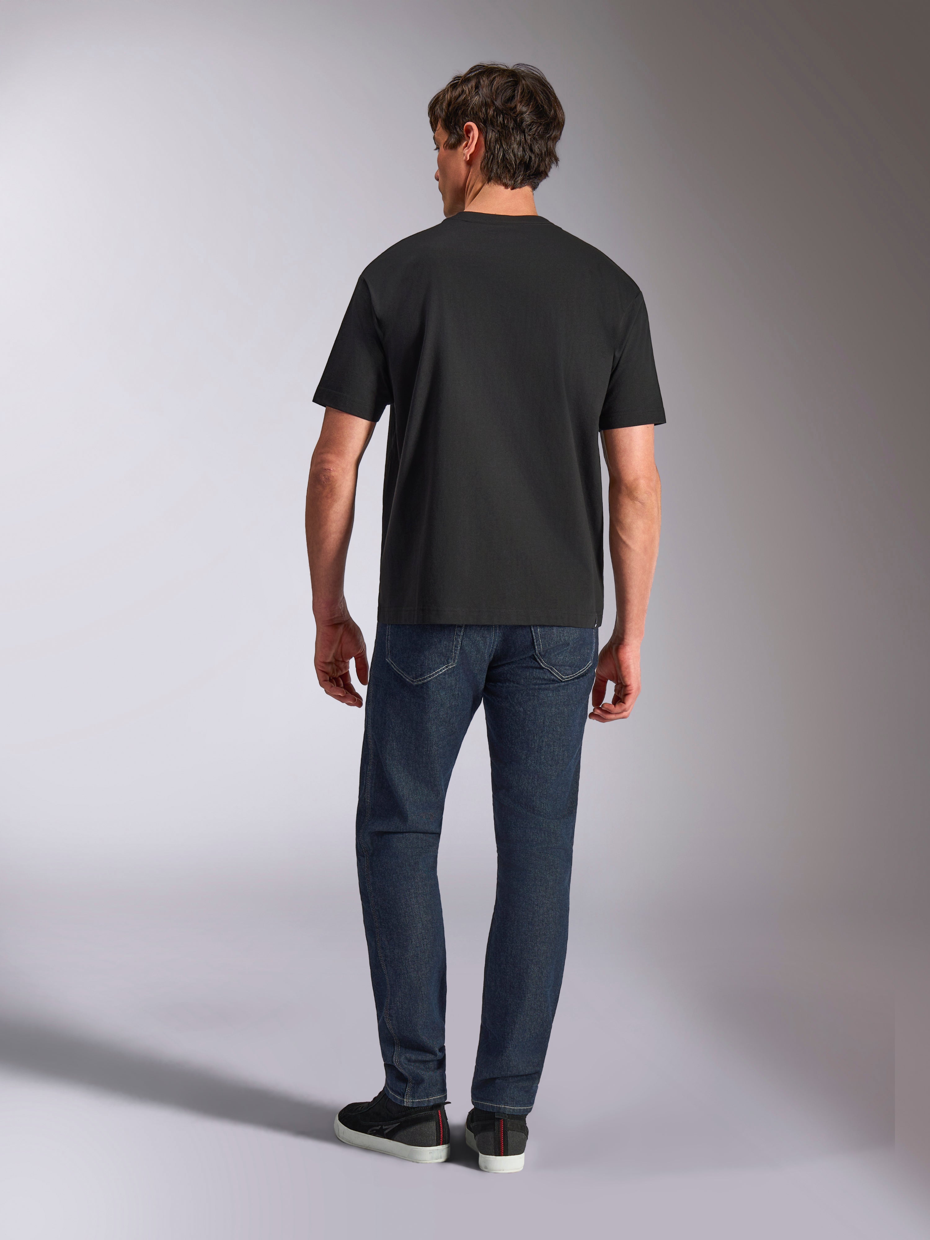 Alpinestars Aplomb Oversized CSF Tee, maglietta a maniche corte, nero, vista posteriore su modello che indossa t-shirt vestibilità rilassata con jeans in denim, abbigliamento streetwear casual motorsport