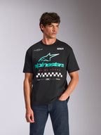 T-shirt Alpinestars Aplomb Oversized CSF, maglietta a maniche corte, nera, con un grande logo combinato Astars verde acqua e bianco e grafica a scacchi, indossata da un modello uomo con jeans blu scuro, stile streetwear casual ispirato al motorsport