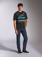 Alpinestars Aplomb Oversized CSF Tee, maglietta a maniche corte, nero, grande logo Alpinestars verde acqua e bianco con gradiente di colore, testo Racing Ahead e motivo a scacchi, indossata con jeans blu scuro e sneakers nere, streetwear casual motorsport