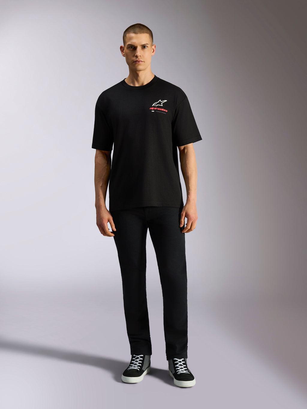 Alpinestars Overhang Oversized CSF Tee, t-shirt a maniche corte, nera, logo Astars bianco con testo rosso, indossata da un modello con pantaloni neri e sneakers, streetwear casual motorsport