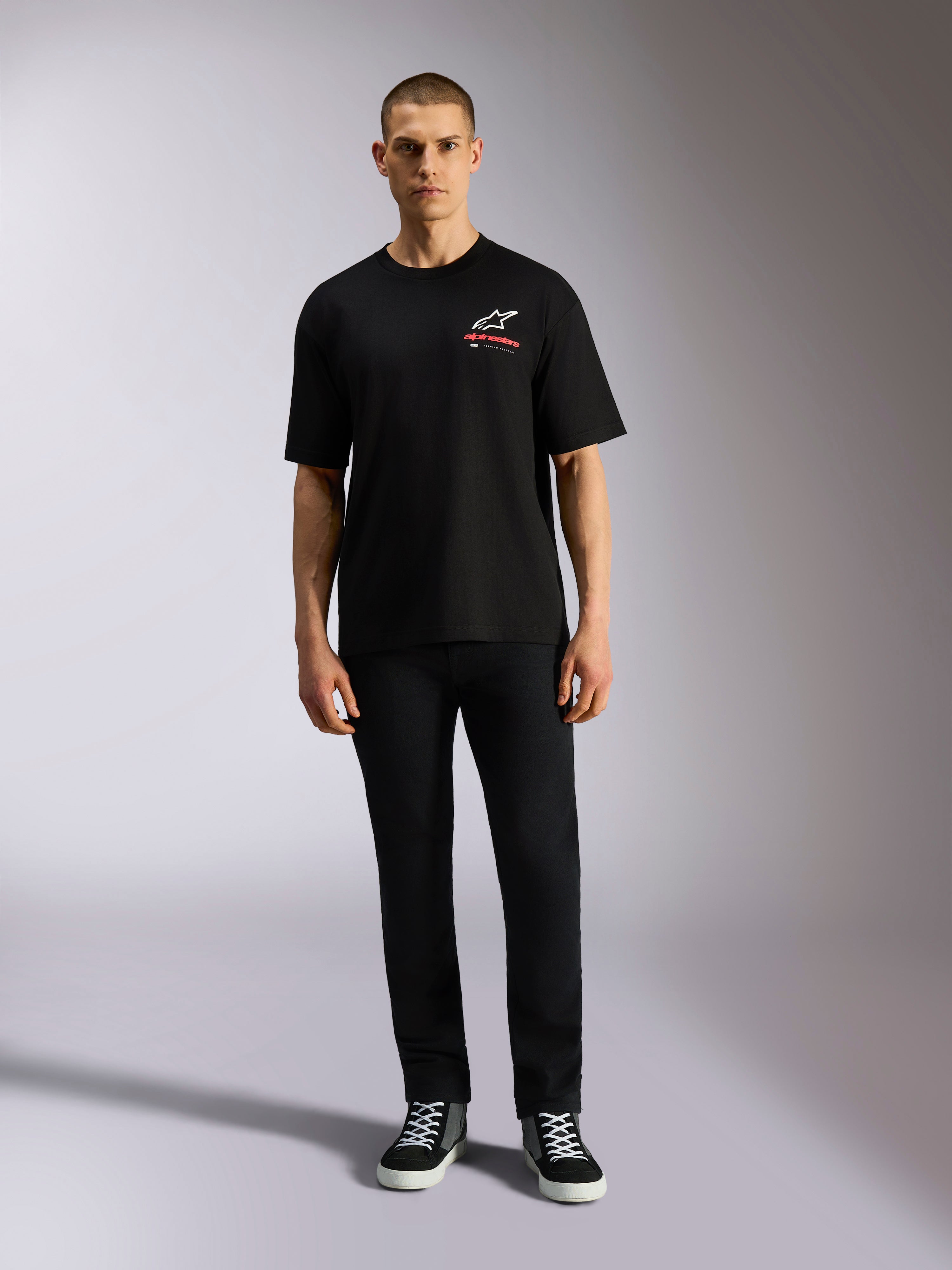 Alpinestars Overhang Oversized CSF Tee, t-shirt a maniche corte, nera, logo Astars bianco con testo rosso, indossata da un modello con pantaloni neri e sneakers, streetwear casual motorsport
