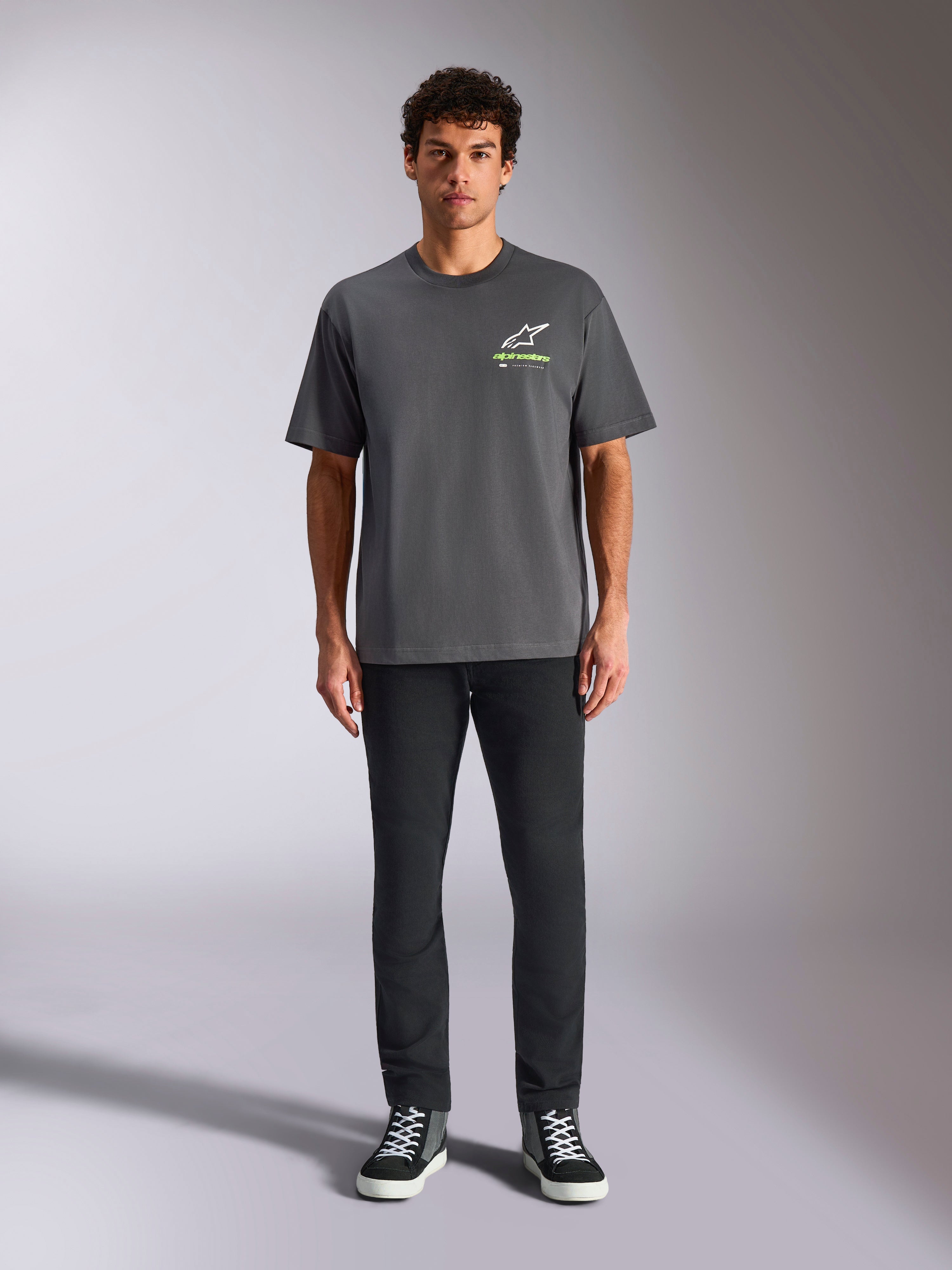 Alpinestars Overhang Oversized CSF Tee, t-shirt a maniche corte, grigio antracite, con logo Alpinestars frontale bianco e verde lime, indossata da un modello con pantaloni neri e sneakers, stile streetwear casual e rilassato