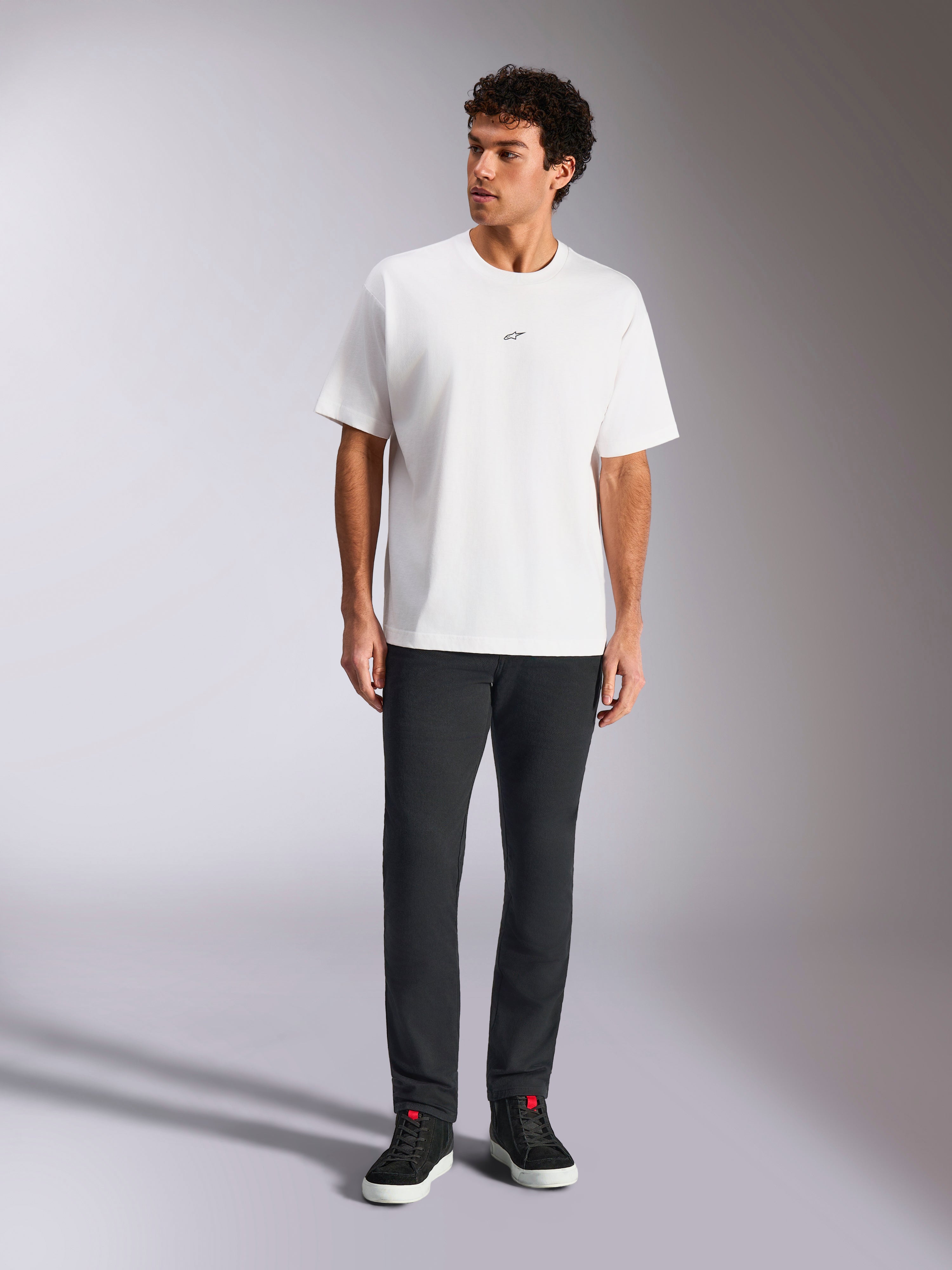 Alpinestars Focused Oversized CSF Tee, t-shirt a maniche corte, bianco, piccolo logo Astars nero sul petto, stile casual streetwear, indossata da un modello con pantaloni scuri e sneakers alte nere