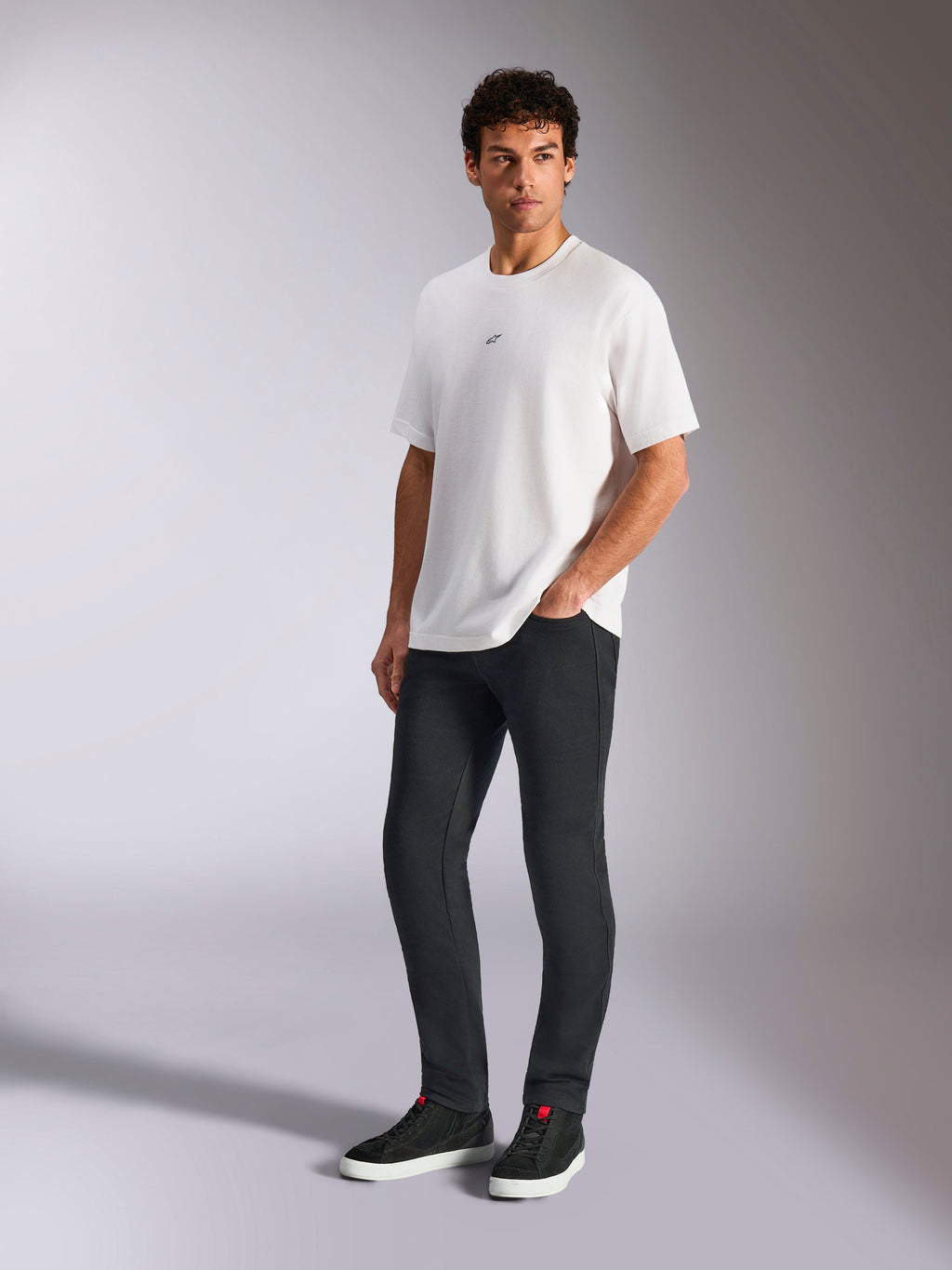 Alpinestars Focused Oversized CSF Tee, t-shirt a maniche corte, bianca, con piccolo logo Astars nero sul petto, indossata da un modello con pantaloni scuri e sneakers nere, streetwear casual ispirato al motorsport