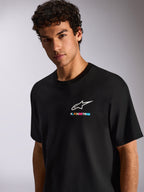 Un uomo indossa la T-shirt Alpinestars Wild Oversized CSF, maglietta nera a maniche corte con logo Astars bianco e branding multicolore vivace sul petto, streetwear casual motorsport