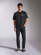 Alpinestars Wild Oversized CSF Tee, t-shirt a maniche corte, nero, indossata da un modello con pantaloni neri e sneakers, con logo Astars bianco e branding multicolore vivace, streetwear casual ispirato al motorsport