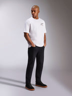 Alpinestars Wild Oversized CSF Tee, maglietta a maniche corte, bianca, con un piccolo logo Astars multicolore sul petto, indossata da un modello con pantaloni neri e sneaker nere, streetwear casual ispirato al motorsport