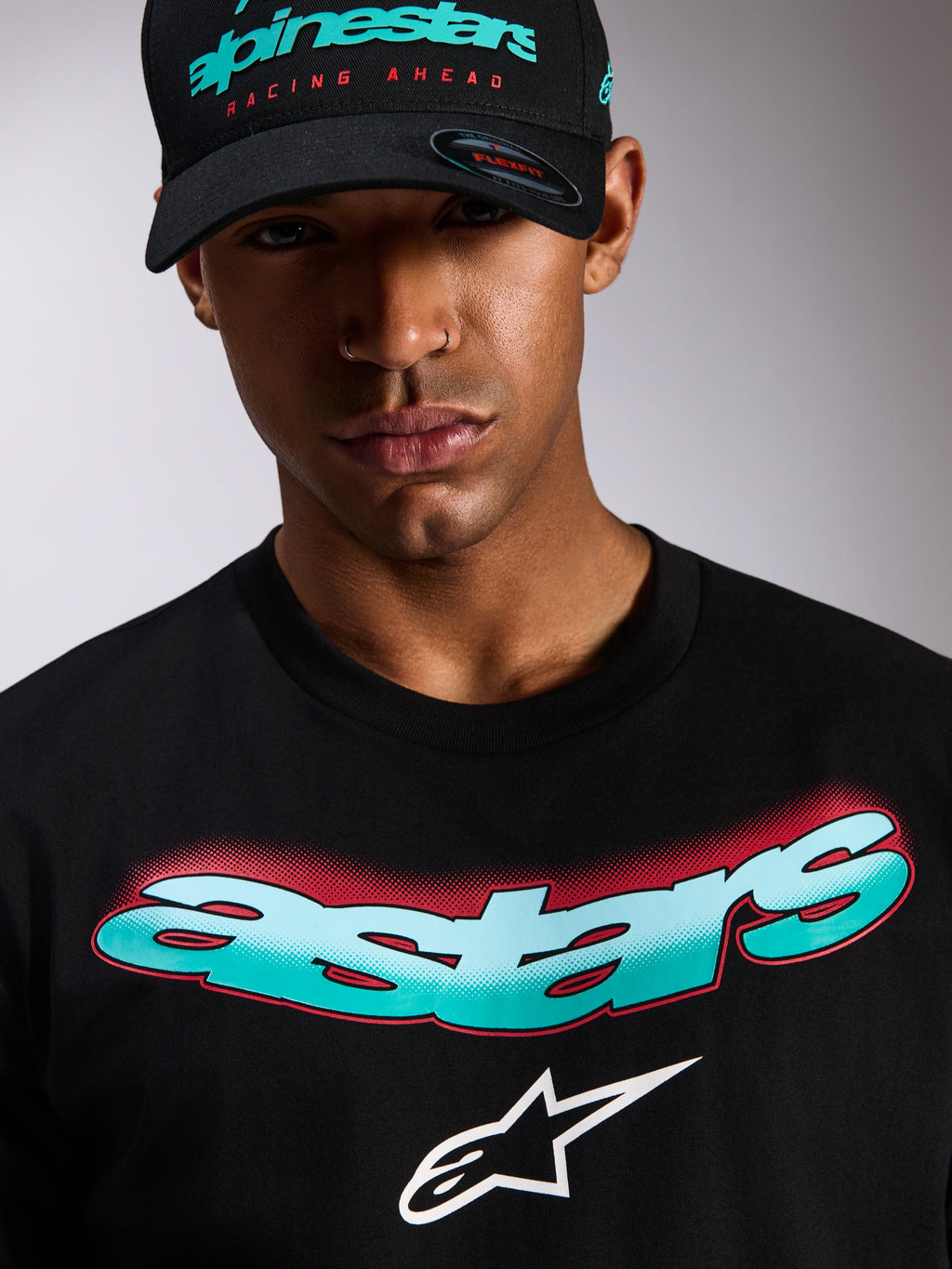 Alpinestars Maglietta Ellipsoid CSF, t-shirt a maniche corte, nera, scritta Astars con gradiente bianco e verde acqua e dettagli halftone rossi, logo Astars bianco, indossata con cappellino Alpinestars nero coordinato, abbigliamento casual motorsport streetwear